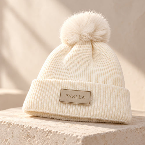 PNELLA cream pom-pom beanie styled on a stone plinth
