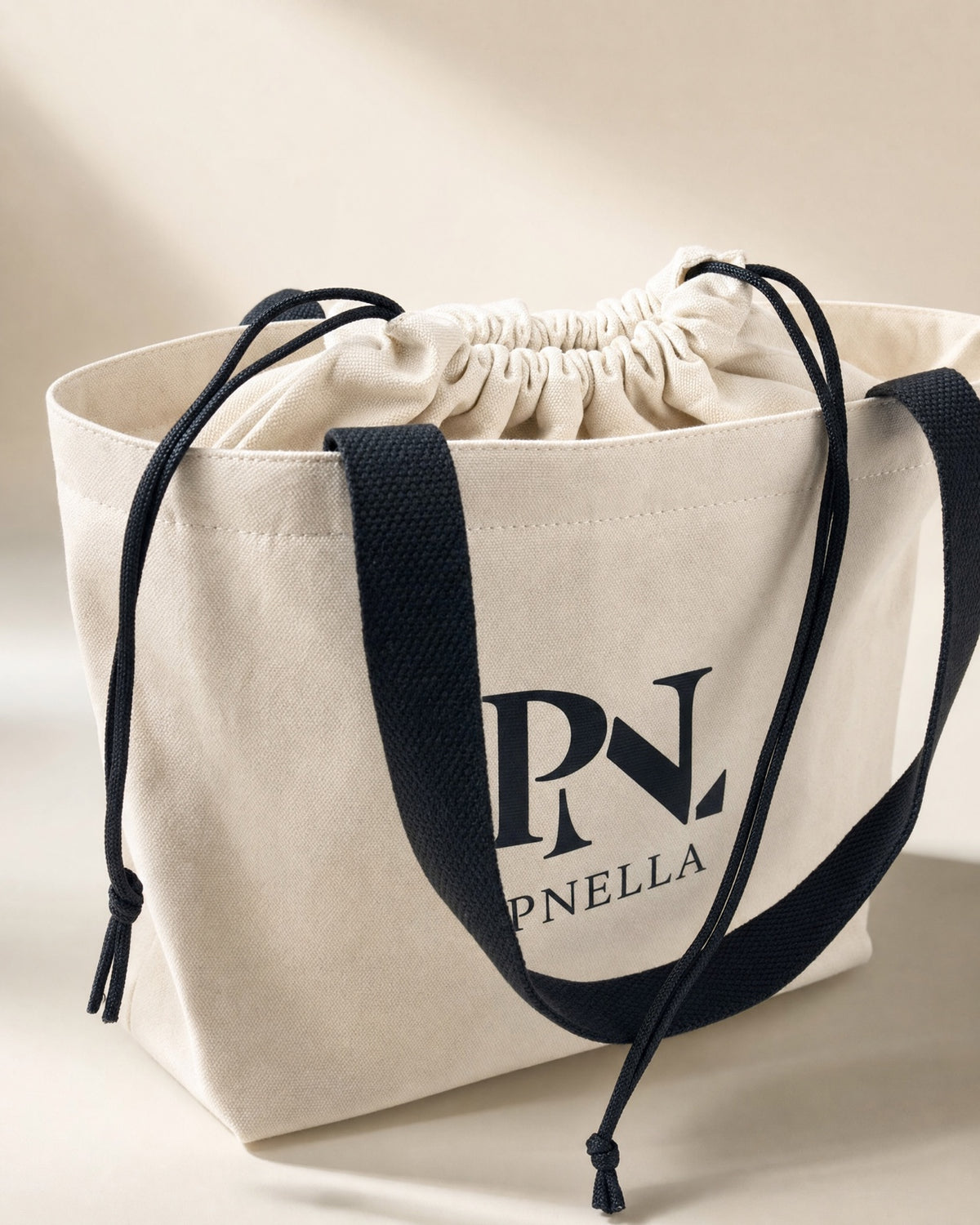 PNELLA signature cream tote bag with black handles and drawstring closure
